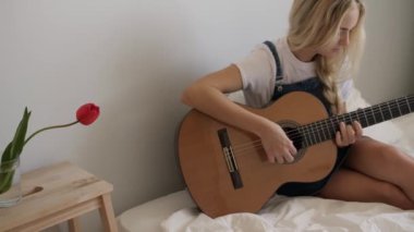Sarışın bir kadın rahat bir yatakta oturur ve doğal ışıkta akustik gitar çalar. Sahne sakinlik ve yaratıcılık yayar, müzik, rahatlama ve yaşam tarzı gibi kavramlar için idealdir..
