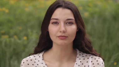 Huzurlu bir kadın yemyeşil ve sarı kır çiçekleriyle çevrili saçlarında hafif bir rüzgarla yemyeşil bir bahar çayırında duruyor. Doğa, yaşam tarzı ve mevsimsel görseller için mükemmel.. 
