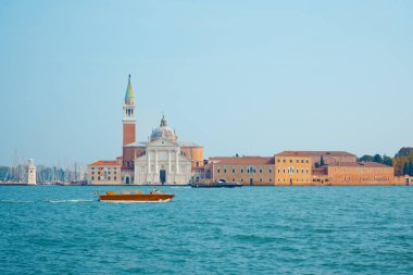 İtalya 'nın Venedik kentindeki San Giorgio Maggiore adasının çarpıcı bir görüntüsü, ikonik çan kulesi, tarihi mimari ve sakin sularda süzülen bir su taksisi. Seyahat temaları için ideal. 