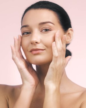 Işıl ışıl, sağlıklı tenli beyaz bir kadın yumuşak pembe bir arka plana nazikçe yüzüne dokunuyor. Reklamlarda cilt bakımı, güzellik ve kendine özen kavramları için mükemmel..