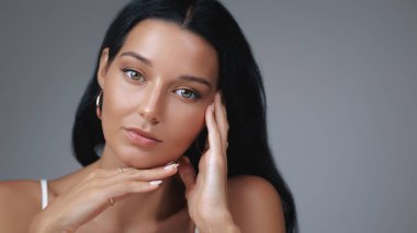 Doğal makyajlı güzel bir kadın, parlayan bir ten ve elinde yüzüyle zarifçe poz veren altın halka küpeler. Cilt bakımı reklamları, güzellik kampanyaları ve yaşam tarzı promosyonları için ideal.. 