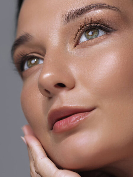Детальный крупный план молодой женщины с блестящими губами и сияющей, безупречной кожей, нежно касающейся ее лица. Идеально подходит для красоты, кожи и рекламы косметических продуктов или учебных пособий.