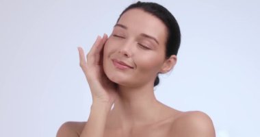 Kusursuz derisi olan güzel bir kadın nazikçe yüzüne ve omzuna dokunuyor ve kendine bakmanın keyfini çıkarıyor. Cilt bakımı, güzellik ve sağlık promosyonları için mükemmel.. 