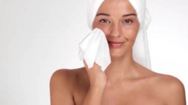 Kafasına havlu sarılmış güzel bir kadın gülümserken hafifçe yüzünü havluyla kurutuyor. Cilt bakımı, kendine özen ve güzellik konseptleri için mükemmel.. 