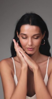 Kusursuz, pırıl pırıl cildi olan, elleri yüzünün yanında zarafetle poz veren güzel bir kadın. Zarafet ve güveni vurgulayan güzellik, cilt bakımı ve moda kavramları için ideal. 