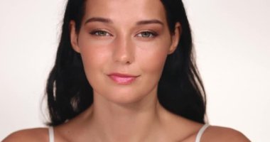 Kusursuz makyajlı, parlak bir stüdyoda hafifçe gülümseyen kendine güvenen bir kadının yakın çekimi. Güzellik, kozmetik ve yaşam tarzı odaklı kampanyalar için ideal.. 