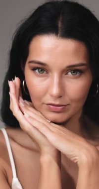 Kendine güvenen bir kadının yakın plan portresi. Parlak bir cildi ve doğal makyajı var. Yüzüne yakın elleriyle zarifçe poz veriyor. Güzellik, cilt bakımı ve kendine özen kavramları için mükemmel.. 