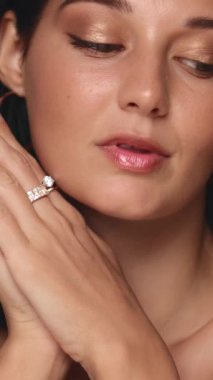 Parlak mücevherler ve doğal makyajla zarif poz veren bir kadının yakın çekimi. Stüdyo ortamında güzellik, moda veya lüks yaşam tarzı ürünlerini tanıtmak için mükemmel.. 