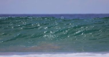 Güçlü okyanus dalgalarının tropik bir plaja çarpmasının yavaş çekim görüntüleri. Turkuaz su, güneşin altında parlayarak büyüleyici ve dramatik bir deniz sahnesi yaratır.. 