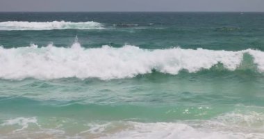 Çarpıcı turkuaz dalgalar kumlu bir sahile yavaş çekimde çarparak doğanın gücünü ve güzelliğini gözler önüne seriyor. Yaz, seyahat ve tropikal tatil görüntüleri için ideal..