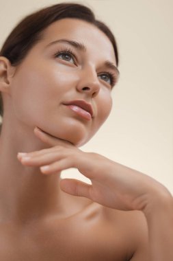 Kusursuz, pırıl pırıl bir cildi olan, sakin bir ifadeyle yukarıya bakan genç bir kadının yakın plan portresi. Cilt bakımı, güzellik, sağIık ve öz bakım içeriği için idealdir.. 