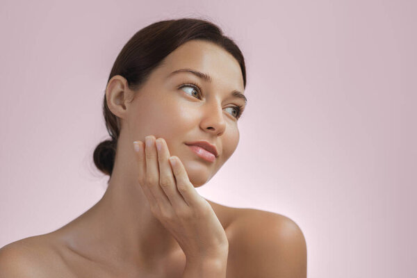 Молодая женщина с сияющей, здоровой кожей нежно касается своего лица, отражая спокойный и расслабленный момент кожи. Идеально подходит для продвижения красоты, скинхеда, велнес и ухода за собой с упором на натуральные продукты