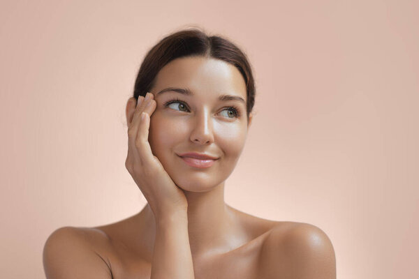 Портрет молодой женщины с светящейся кожей, нежно положившей руку на лицо и улыбающейся. Идеально подходит для продвижения красоты, скинкара и косметики. Высококачественное изображение, демонстрирующее природную красоту и