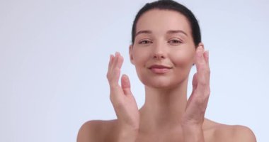 Neşeli, genç, beyaz bir kadın. Işıl ışıl, sağlıklı bir teni var. Gözleri kapalı gülümsüyor, nazikçe yüzünü tutuyor. Güzellik, sağlık ve lüks cilt bakımı kampanyaları için mükemmel.. 