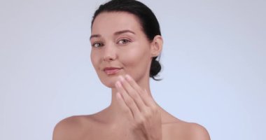 Çıplak makyajlı güzel bir kadın yüzüne nazikçe losyon sürüyor doğal güzelliğini ve parlak cildini sergiliyor. Bu yüksek kaliteli video cilt bakımı, spa ve sağlık konseptleri için mükemmel. İdeal