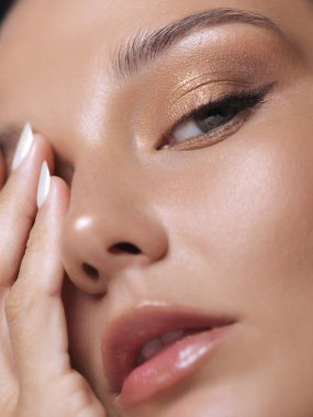 Kusursuz cilt, parıldayan göz makyajı ve parlak dudaklar sergileyen genç bir kadının aşırı yakın çekimi. Reklam ve tanıtımlarda güzellik, makyaj ve cilt konseptleri için ideal. 
