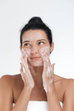 Genç Asyalı bir kadın yüzünü köpüklü bir yüz temizleyiciyle temizliyor, cilt bakımını, hijyeni ve kendine bakımı teşvik ediyor. Güzellik, sağlık ve kişisel bakım ürünü reklamları için ideal.. 