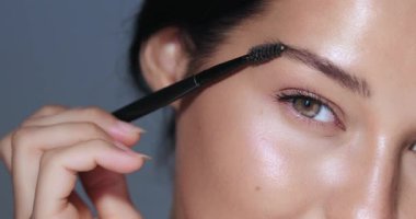 Kaşlarını tanımlamak için makyaj fırçası kullanan genç bir kadının parlak cildini ve kusursuz güzelliğini ön plana çıkardığı yakın çekim. Güzellik, kozmetik ve makyaj uygulama kavramları için ideal.