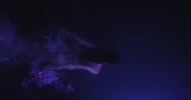 Şehvetli bir kadın mor ışıklı bir havuzda karanlık sularda süzülerek sanatsal ve gerçeküstü bir sahne yaratıyor. Zarif hareketi ve zarif silueti kompozisyona gizem ve güzellik katıyor.. 