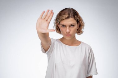 Beyaz tişörtlü beyaz bir kadın ciddi bir ifadeyle dur hareketi yaparak elini öne uzatıyor. Reddetme, reddetme, sınırlar veya protesto temaları için kavramsal görüntü.