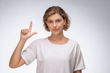 Beyaz tişörtlü kendine güvenen bir kadın, arka planda ciddi bir ifadeye işaret ediyor. Bu yüksek kaliteli görüntü yön, liderlik ve odaklanma kavramlarını aktarmak için idealdir.