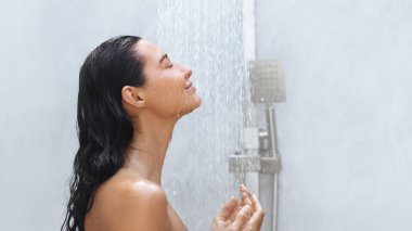 Gözleri kapalı sakin bir kadın, duş sırasında suyun yumuşak akışının tadını çıkarır. Onun barışçıl ifadesi rahatlama ve kendine bakmanın özünü yakalıyor ve bu imajı terfi için mükemmel kılıyor.