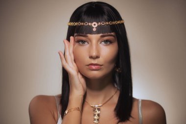 Kleopatra 'dan esinlenilmiş altın başlık ve kolyeyle süslenmiş uzun siyah saçlı zarif bir kadın. Bu çarpıcı görüntü güzellik, moda ve lüks temalar için idealdir..