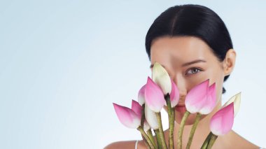 Zarif bir kadın yüzünün yanında bir buket pembe nilüfer tomurcuğu tutuyor doğal güzellik ve cilt bakımı sergiliyor. Spa tedavileri, güzellik ürünü reklamları ve lüks cilt bakımı için mükemmel.