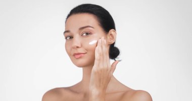 Kusursuz cildine nazikçe nemlendirici krem süren genç bir kadın güzelliği, cildini ve sağlığını simgeliyor. Kozmetik ve kişisel bakım promosyonları için mükemmel.. 