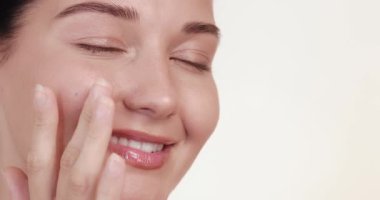 Güzel beyaz bir kadının gülümsemesi ve cilt kremini yavaş çekimde sürmesi. Kozmetik ürünleri, nemlendirici reklamlar, yüz bakımı, güzellik rutinleri veya serum promosyonları için ideal.
