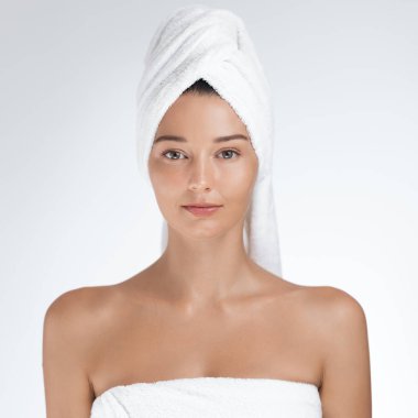 Işıl ışıl bir teni olan, yumuşak beyaz bir havluya sarılmış, sakince bakan güzel bir genç kadın. Doğal güzelliği ve rahat ifadesi bunu cilt bakımı, sağlık ve kaplıca kavramları için mükemmel bir görüntü yapıyor..