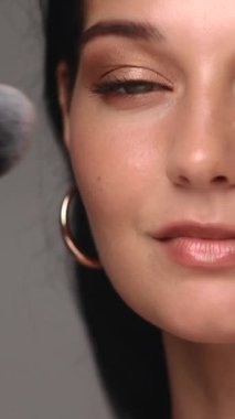 Siyah saçlı genç bir kadın, yumuşak bir toz fırçası kullanarak güzelliğini arttırır. Kusursuz cildi, ince göz makyajı ve kendine güveni bunu güzellik, cilt bakımı ve...