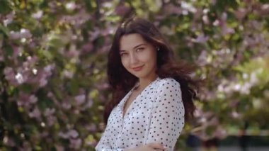 Uzun siyah saçlı genç bir kadın çiçek açan kiraz çiçekleriyle dolu bir bahçede dururken nazikçe gülümsüyor. Sahne, ilkbahar güzelliğini, doğayı ve dinginliği temsil eder..