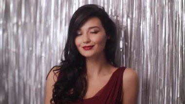 Koyu kırmızı elbiseli çekici esmer, gümüş bir perdenin önünde neşeli bir gülümsemeyle göz kırpıyor. Flört eden moda reklamları, makyaj reklamları ve romantik ya da gece hayatı kavramları için ideal..