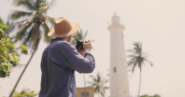 Şapkalı bir gezgin Sri Lanka 'daki Galle Fort deniz fenerinin fotoğraflarını çekiyor. Bu yüksek kaliteli video keşif ve seyahat ruhunu yansıtıyor, turizm reklamları, seyahat blogları ve