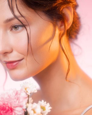 Beyaz tenli, sıcak tonlu, elinde çiçekler olan beyaz bir kadının yakın plan stüdyo portresi. Güzellik kampanyaları, kozmetik reklamları, cilt tanıtımları ve görsel sağlıklar için ideal..