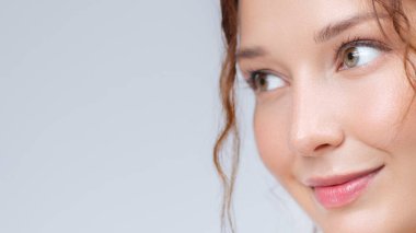 Parlak bir teni ve parlak dudakları olan genç ve güzel bir kadın nazikçe gülümsüyor. Cilt bakımı, güzellik, sağlık ve doğal kozmetik markaları için ideal..