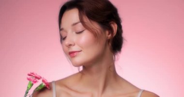 Pembe karanfillerle poz veren beyaz tenli güzel bir kadının yavaş çekim stüdyosu videosu. Güzellik, cilt bakımı, parfüm, çiçek yaşam tarzı ve kozmetik kampanyaları için mükemmel..