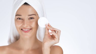 Başının etrafına havlu sarılmış gülümseyen bir kadın, rutin cilt bakımında pamuk tutuyordu. Güzelliği, kendine bakımı, yüz bakımını ve sağlıklı cilt bakımını teşvik etmek için ideal..