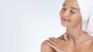 Havluya sarılmış genç bir kadın, gözleri kapalı ve nazikçe omzuna dokunuyor, cilt bakımı rutininden sonra rahatlamanın tadını çıkarıyor. Güzelliği, sağlığı ve spa tedavisini desteklemek için mükemmel.