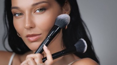 Güzel bir kadın iki farklı makyaj fırçası sergiliyor. Dekoratif kozmetik alanında çok yönlülüğü ve tercihi vurguluyor. Güzellik markaları, kozmetik ürünleri promosyonları ve makyaj dersleri için mükemmel bir imaj..