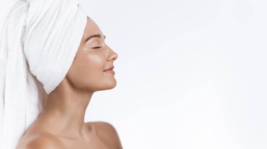 Saçı havluya sarılı, dingin bir kadın gözlerini kapatıyor ve duştan sonra huzurlu bir anın tadını çıkarıyor. Cilt bakımını, sağlık bakımını veya spa tedavisini desteklemek için idealdir, rahatlamayı ve