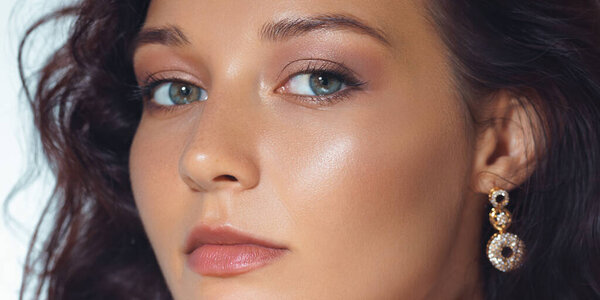Stylish close-up studio portrait of a young woman with perfect makeup, luminous skin, and sparkling earrings. Ideal for cosmetic industry, skincare ads, and beauty branding.