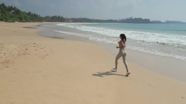 Talalla Sahili, Sri Lanka 'da koşan sağlıklı bir kadının yavaş çekim görüntüleri. Fitness, yaşam tarzı, seyahat, sağlık veya tropikal tatil tanıtımı gibi kavramlar için idealdir..