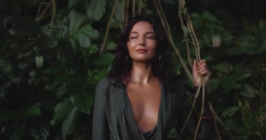 Şehvetli bir kadın tropik orman sarmaşıklarıyla çevriliyken derin bir Ziyaretçi elbisesi içinde poz verir. Bu tarz sinematik görüntüler moda, güzellik ve egzotik yaşam tarzı tanıtım içeriği için mükemmeldir..