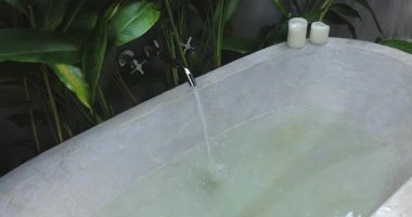 Suyla dolu, yemyeşil bitkiler ve mumlarla çevrili, huzurlu, spa benzeri bir ortam yaratan, rahatlatıcı bir taş küvet sahnesi. Rahatlık ve rahatlama kavramları için mükemmel..