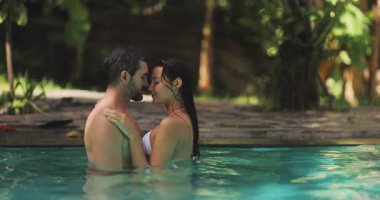 Romantik bir çift, yemyeşil yemyeşil bir havuzda öpüşür. Bu yüksek kaliteli stok videosu bir aşk ve yakınlık anı yakalıyor, romantizm, tatil ve...