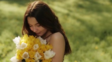 Güneşli bir bahçede bir buket lale tutan ve koklayan dingin genç bir kadının yakın çekimi. Kadınlık, güzellik, bahar tazeliği, sağlık ve doğal yaşam gibi kavramlar için idealdir..