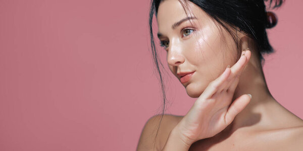 Элегантная фотография азиатки с безупречной кожей и натуральным макияжем, изящно позирующей на розовом фоне. Идеально подходит для кожи, красоты и косметики.