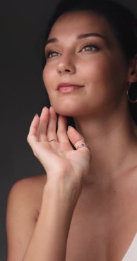 Işıl ışıl cildi ve altın makyajlı güzel bir kadının zarif yakın çekimi, yüzünü hafifçe okşuyor. Cilt bakımı ya da kozmetik reklamları için çok kaliteli bir görüntü..